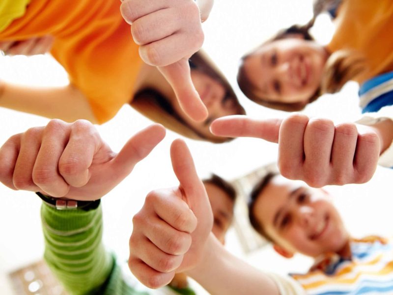 Below angle of happy teens showing thumbs up
